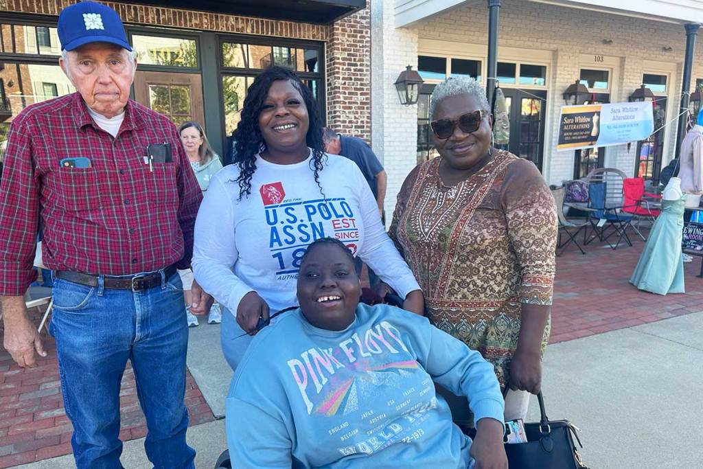 A group of people, one in a wheelchair, pose for a photo together outside of some shops