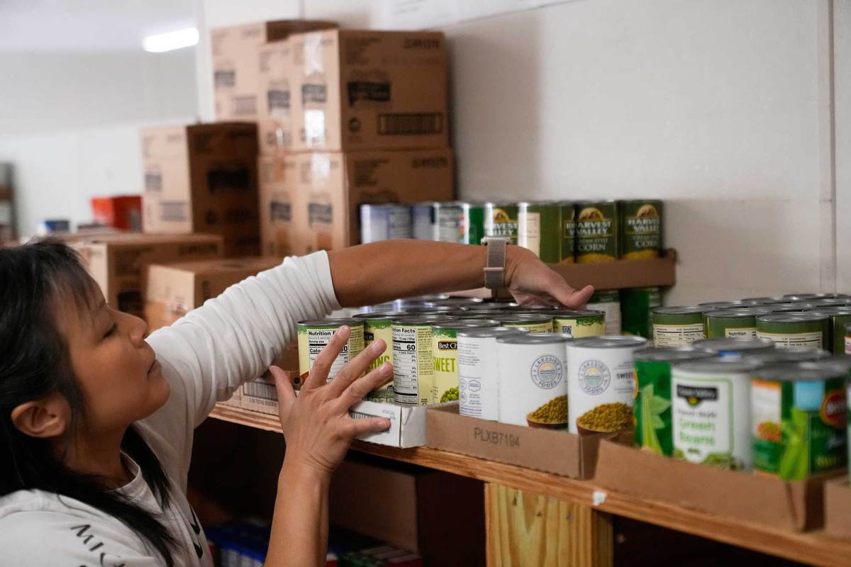 A woman reaches on a tall shelf to sort flats of canned food