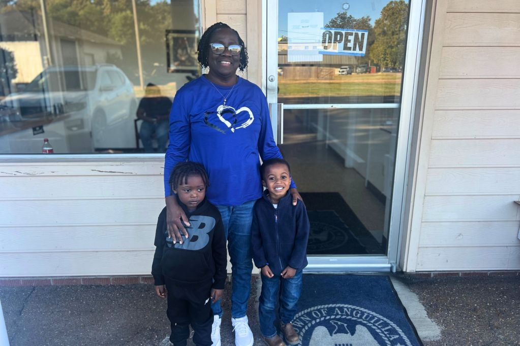 A lady and two children smile outside a building