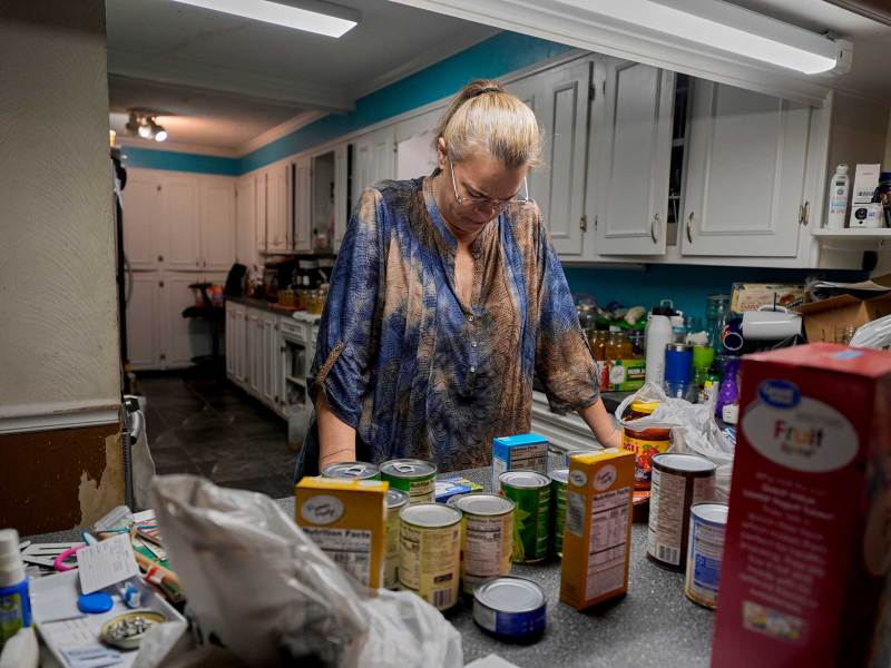 A woman wearing a blue and gold dress with her hands on a kitchen counter. Various grocery and food items are on the counter.