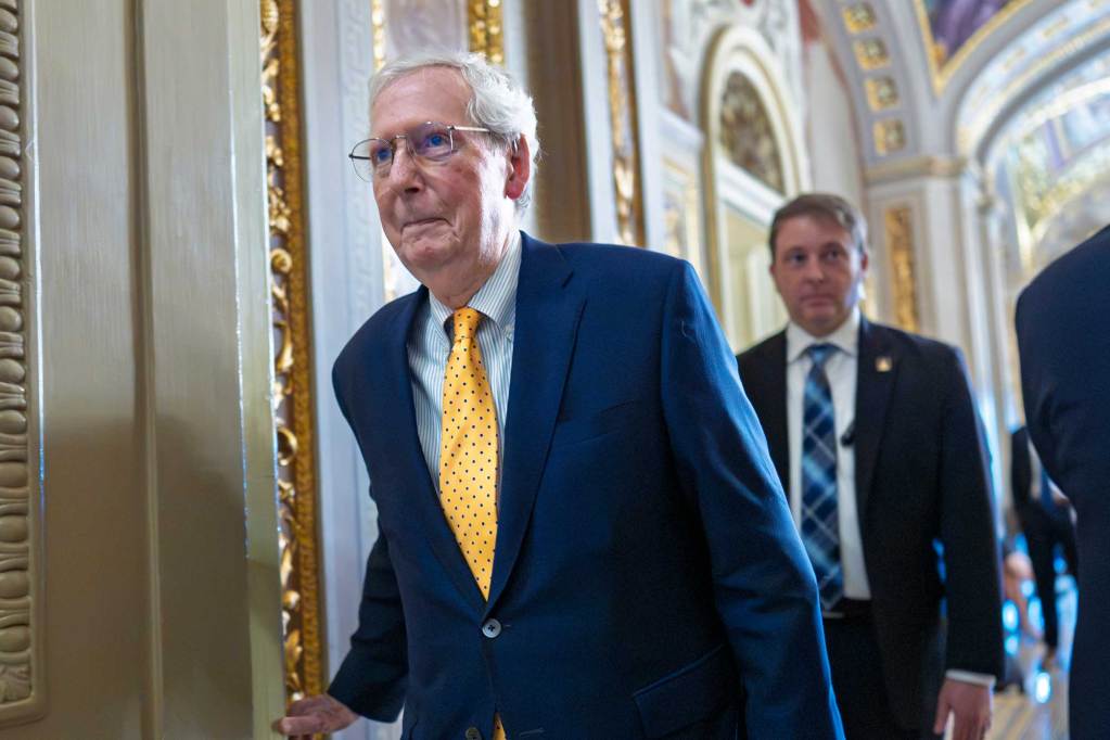 Mitch McConnell walks down the White House hallway with others walking behind him
