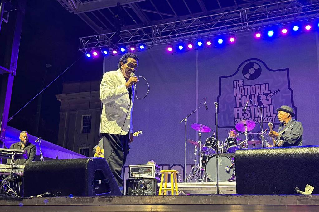 Bobby Rush performs on stage, a sign for the National Folk Festival visible behind him