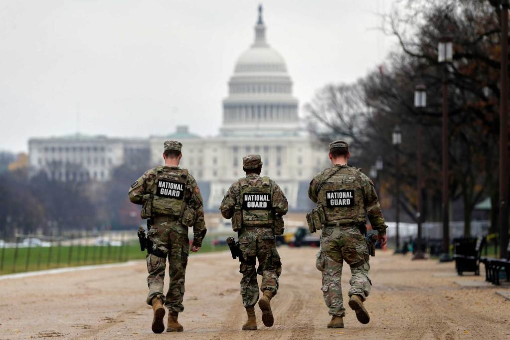 Three National Guardsmen walking toward the U.S. Capitol building. Each is wearing camouflage gear with signs that say “National Guard.”