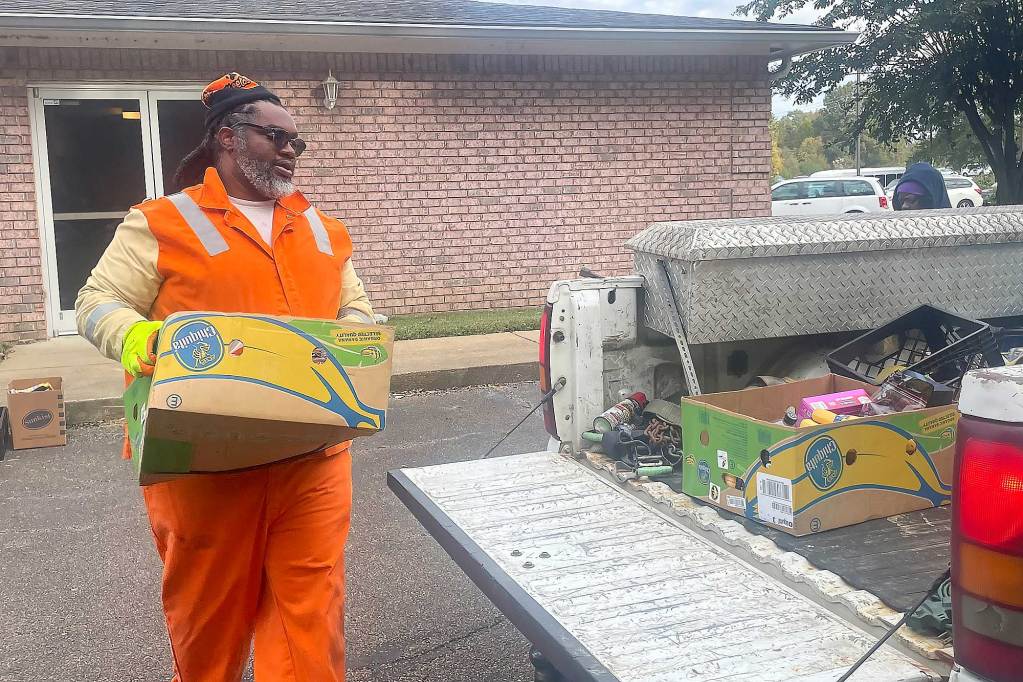 A man in an orange jumpsuit helps carry boxes of food to a truck