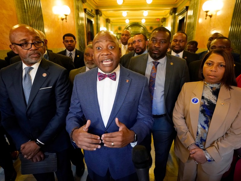 A group of mostly black lawmakers, with one man in the center speaking with his hands out