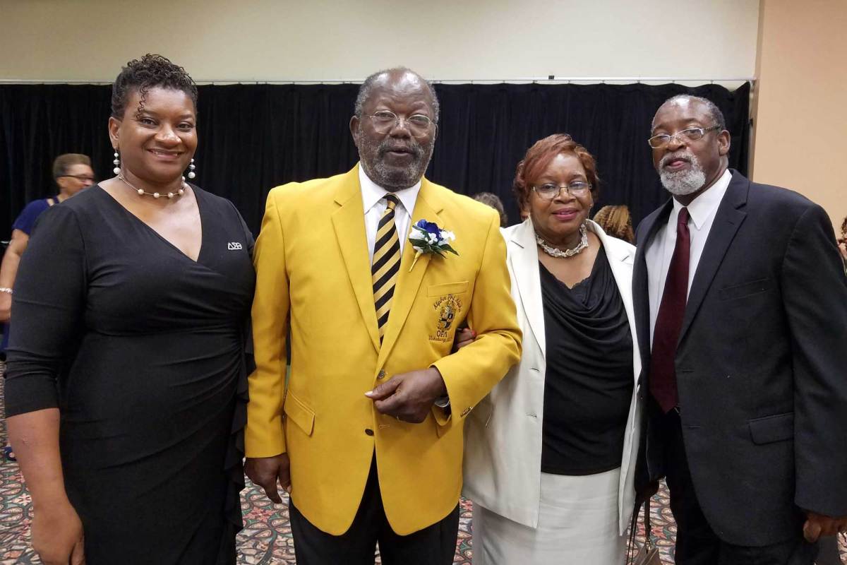 A man in a yellow jacket with yellow and black striped tie poses with two women and another man