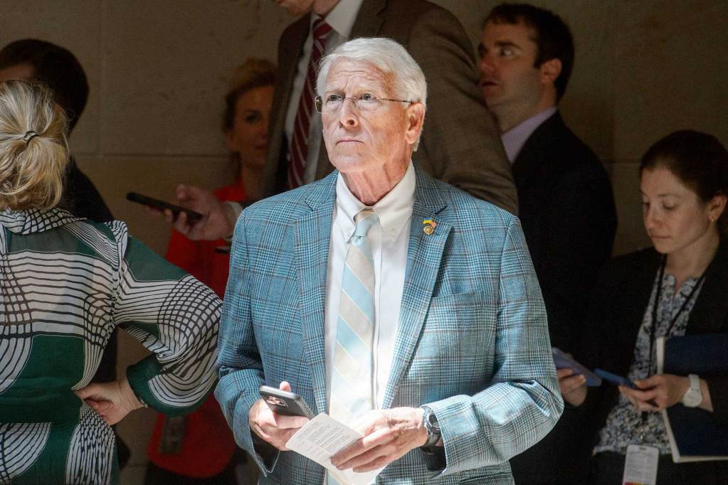 Roger Wicker standing inside in front of a crowd, holding his phone in one hand and a piece of paper in the other