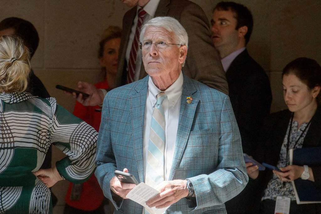 Roger Wicker standing inside in front of a crowd, holding his phone in one hand and a piece of paper in the other