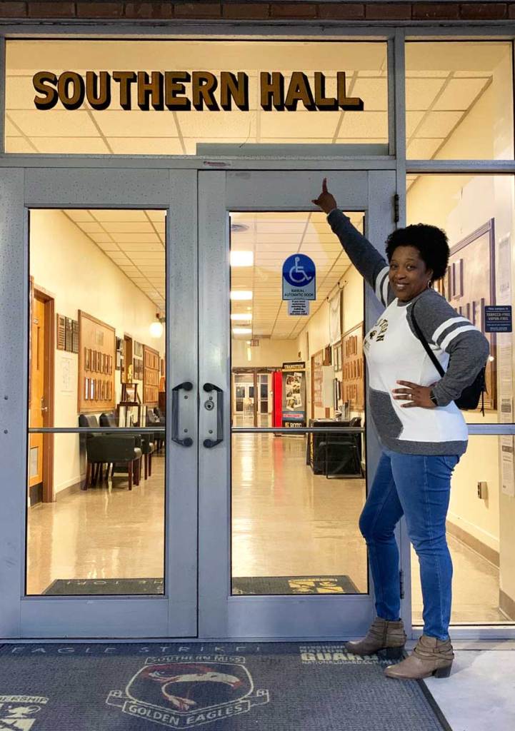 Torsheta Jackson standing in front of college building pointing at sign that reads ‘Southern Hall’