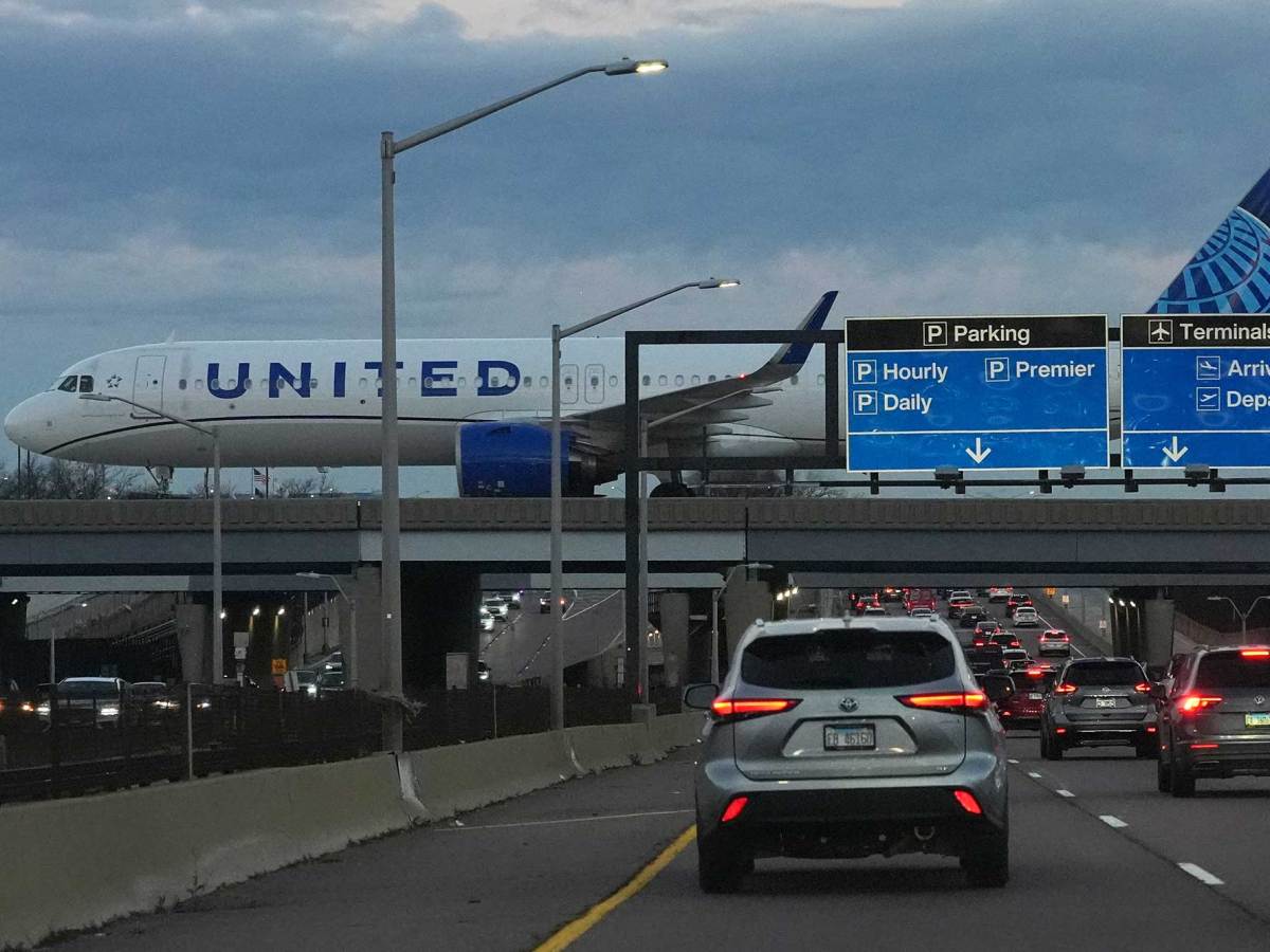 A United Airlines flight lands on a runway. Cars drive under the elevated runway.
