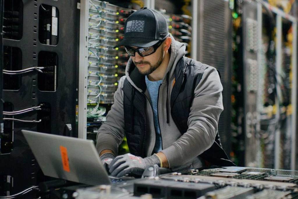 An IT person works on a laptop inside a server room