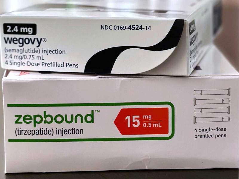 Two packages of medication stacked on top of one another. The top box reads “Wegovy” and the bottom box reads, “Zepbound.”