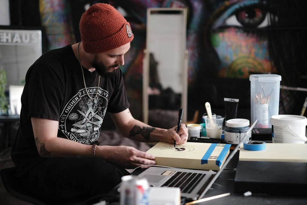 A man in black shirt and red beanie hat drawing on a book cover with a black marker inside an art studio