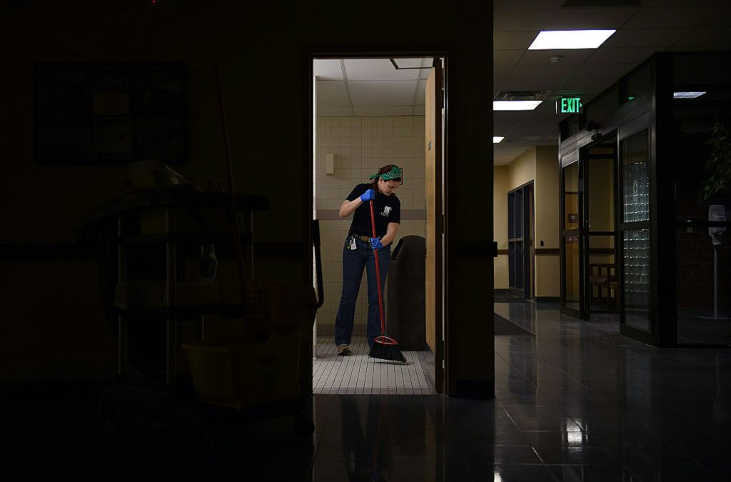 A dark hallway in a hospital with a young woman mopping the floor.