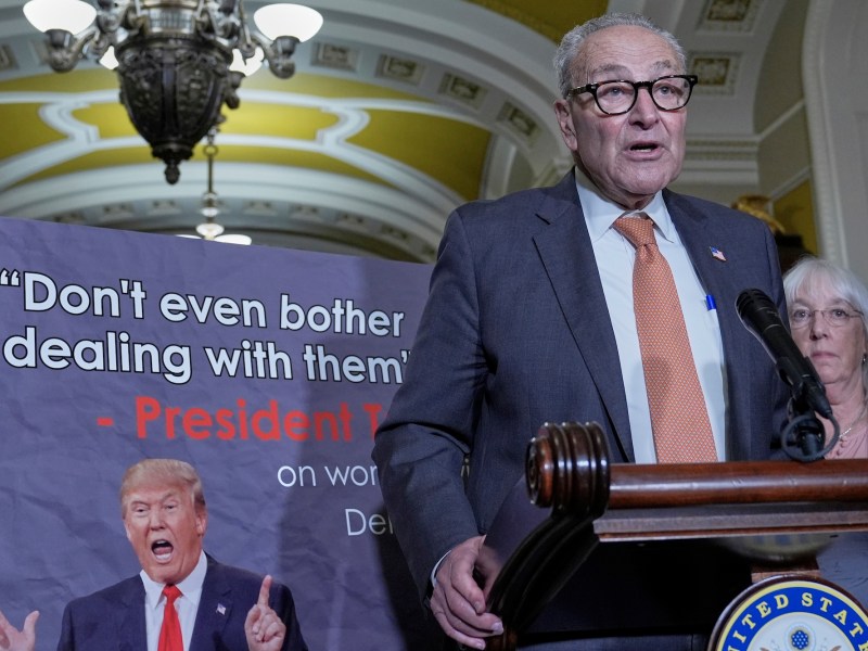 a photo shows Chuck Schumer standing in front of a sign that has a picture of the trump and the words "Don't even bother dealing with them" -Donald Trump