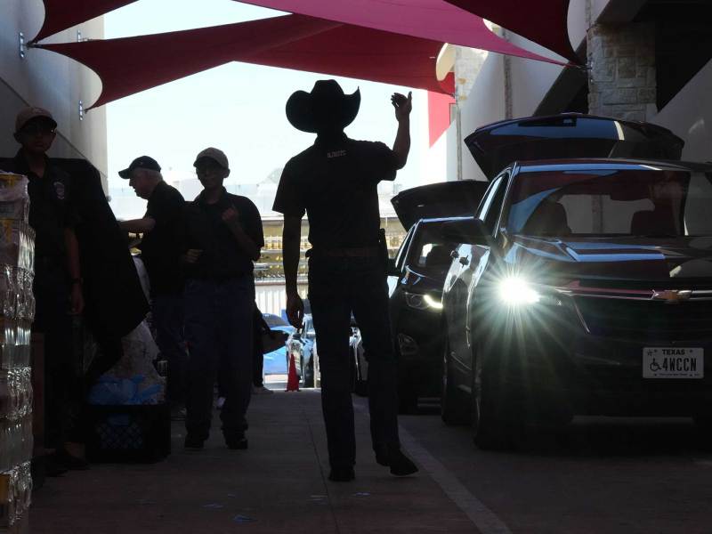 A man in a cowboy hat directs cars to come forward in a tunnel. Other men to his left are organizing supplies.