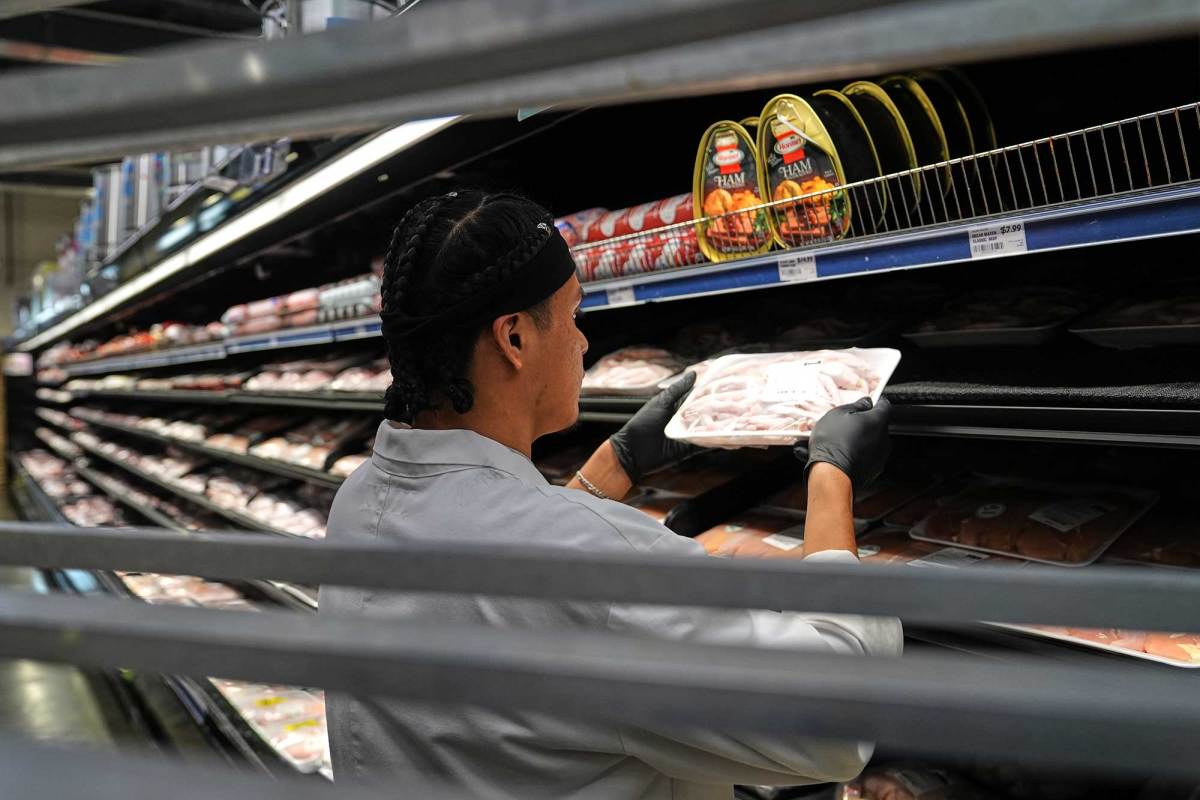A person shelves packaged meat into a cold case in a grocery store