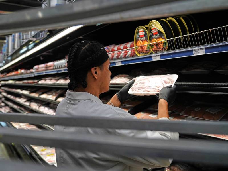 A person shelves packaged meat into a cold case in a grocery store