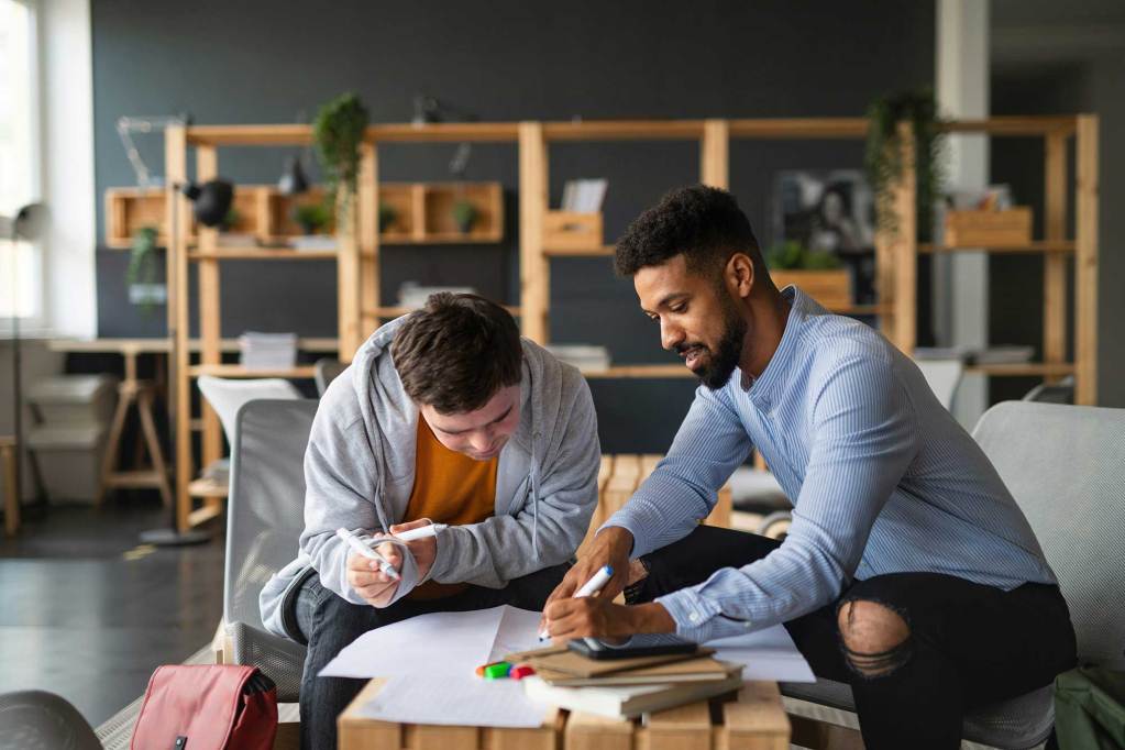 Two men seated at a table, each holding markers as one man tutors the other