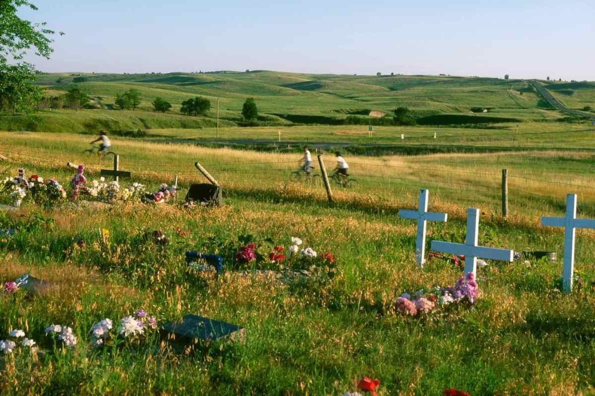 Children riding bikes in the background of an open, grassy field with several white crosses installed in the ground.