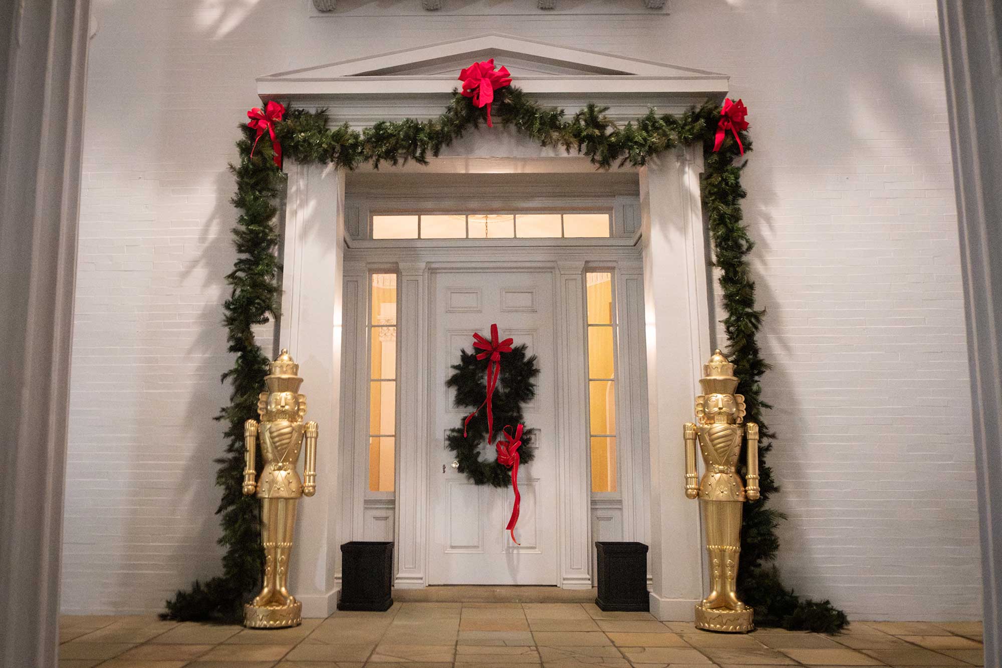 The front door of the Mississippi Governor's Mansion, lit up at night and decorated for Christmas with golden nutcrackers standing on either side of the door