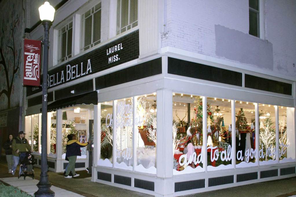 An exterior view of a downtown business on the corner with lit windows filled with a Christmas display