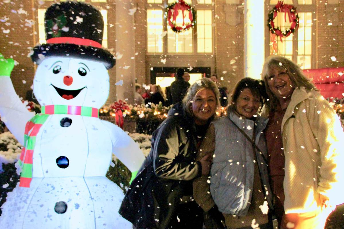 Three people stand together outside next to a lit up Snowman decoration
