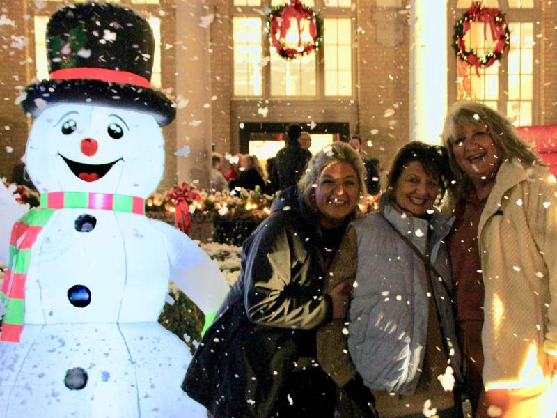 Three people stand together outside next to a lit up Snowman decoration