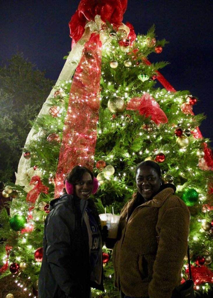 Two people stand outside at night in front of a brightly lit Christmas tree