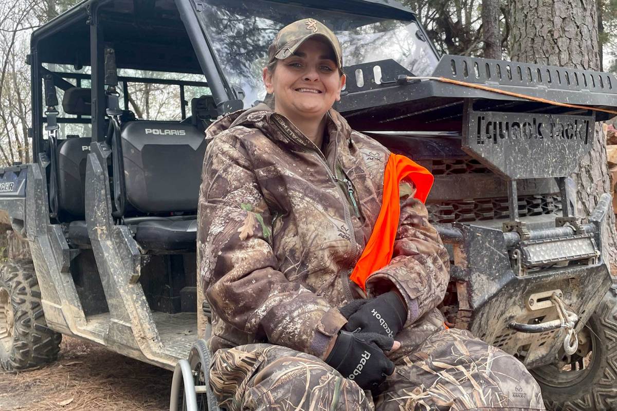 A person in hunting camo sits in their wheelchair in front of a off road vehicle
