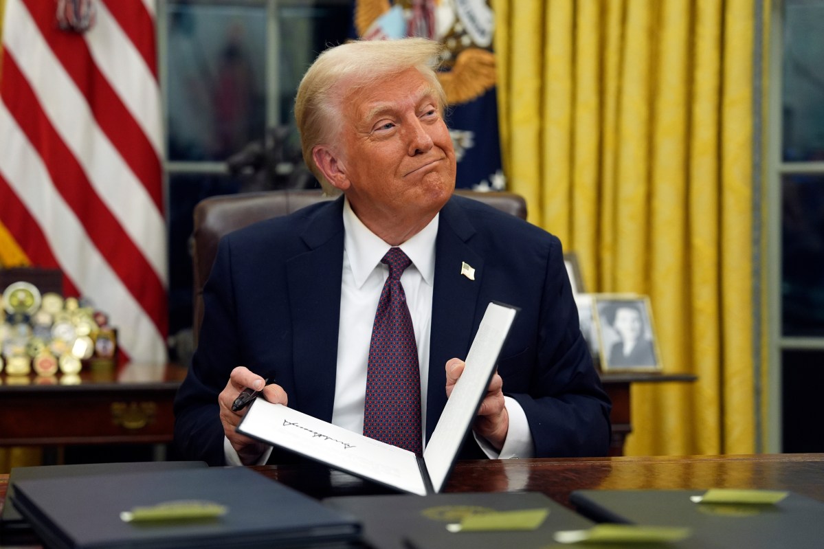 President Donald Trump smiling at his desk in the Oval Office as he closes a folder.