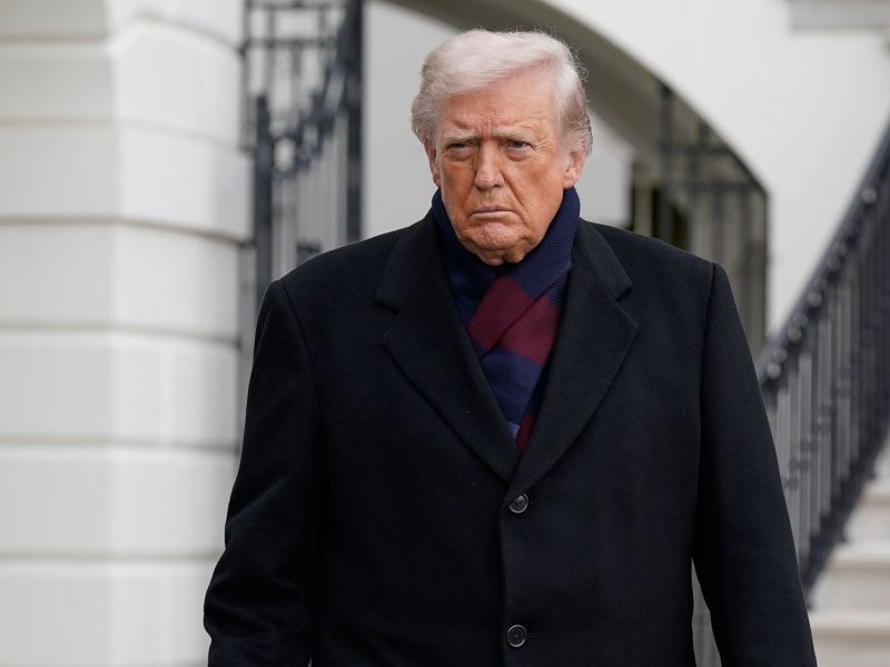 Donald Trump walking outside of the White House wearing a scarf and black coat