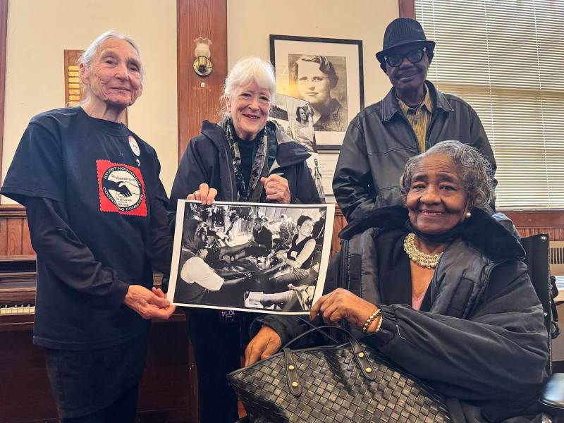 Four people, including Dr. June Finer and Doris Wilson, hold up an old black and white photo of themselves