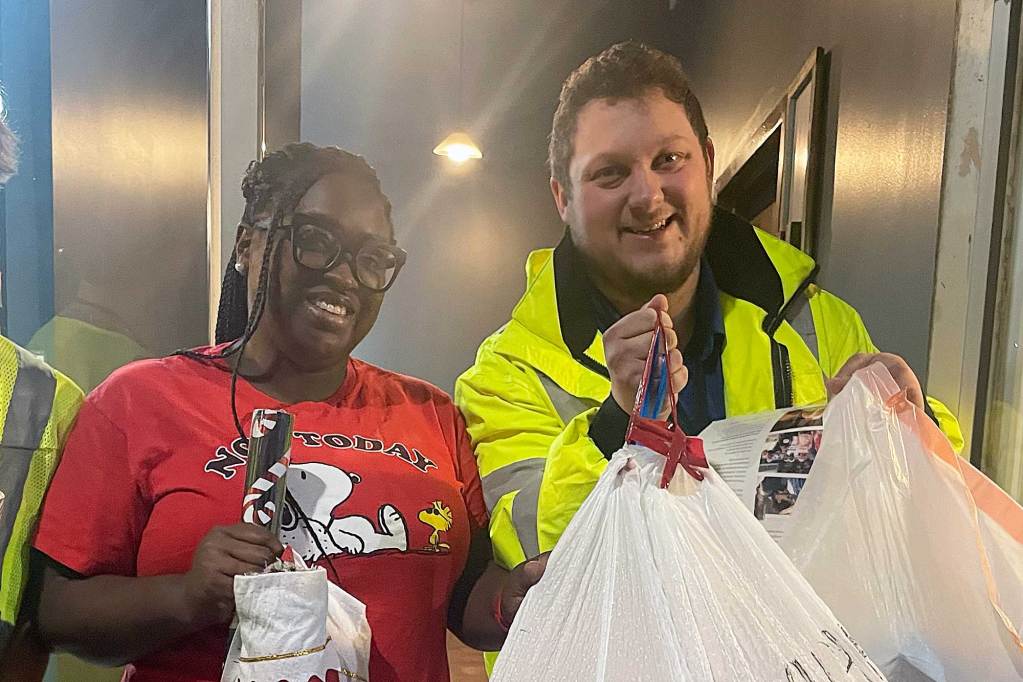 Two people hold up stockings and bags of gifts