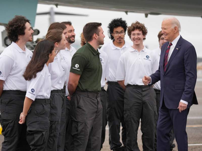 President Joe Biden greeting several young people. One is in a dark green shirt and the rest are wearing white shirts.