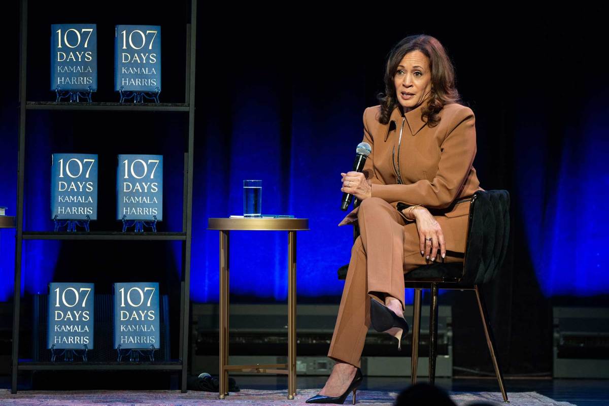 Kamala Harris sits on a stage and speaks next to a display of her book '107 Days'