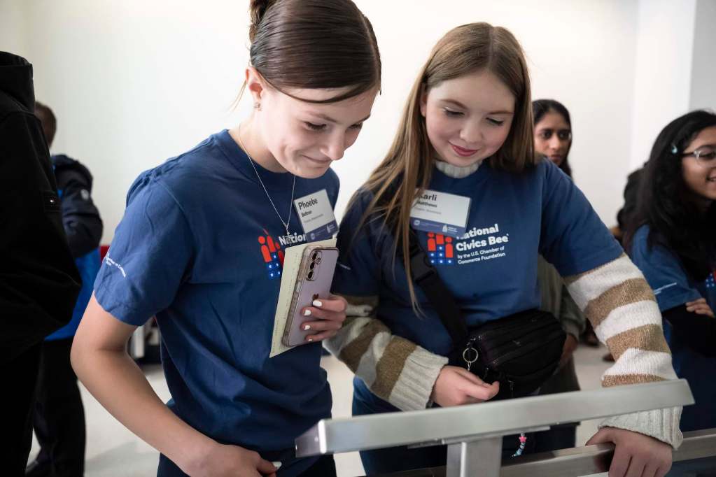 Two young women in matching blue tshirts that read "National Civics Bee" read a display together