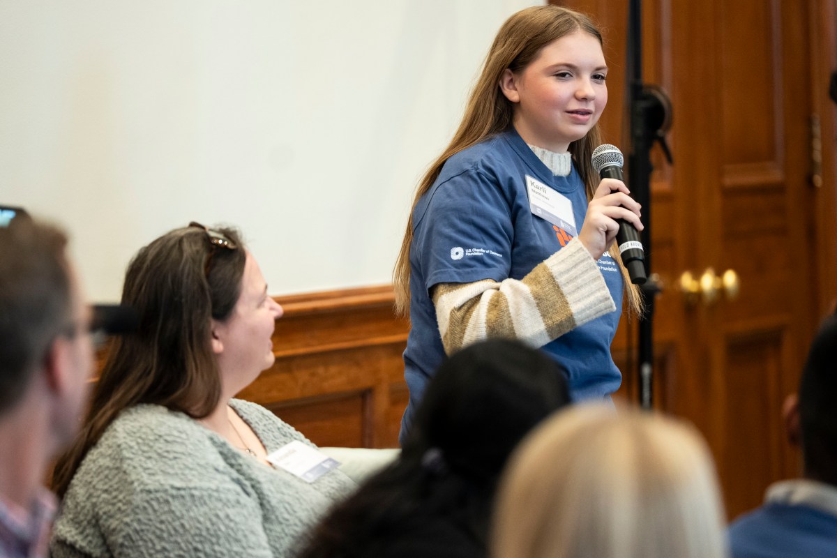 A young woman holds up a mic and speaks to a room at a Civics Bee
