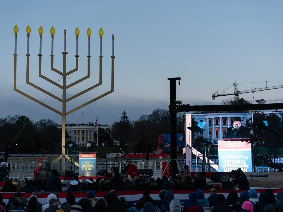A stage outside with a large Menorah display, the White House visible in the background.