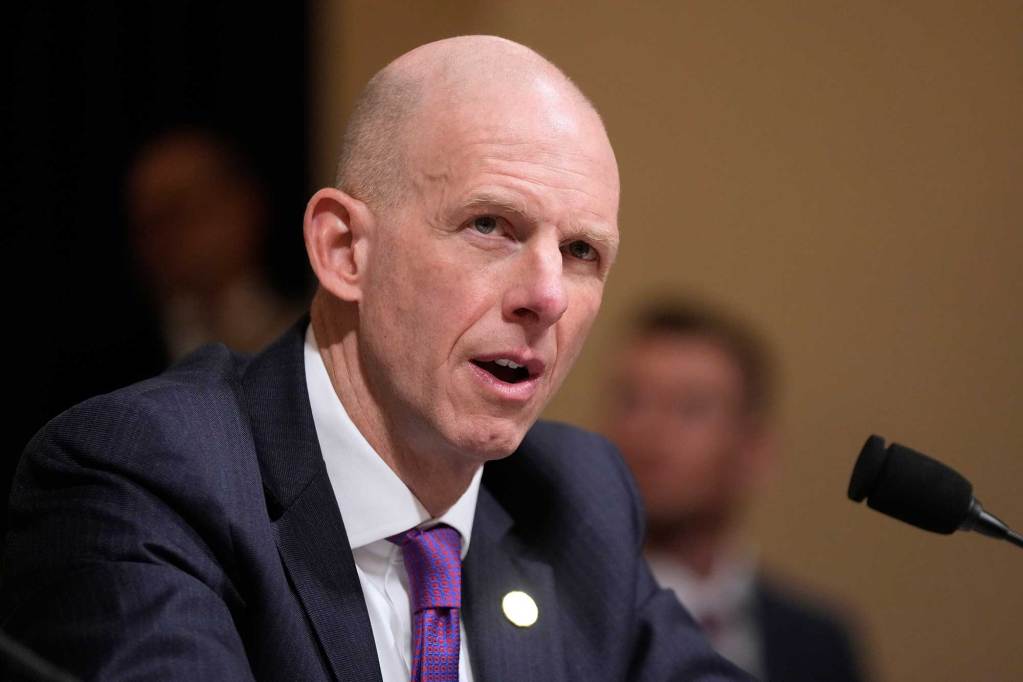 A bald man in a suit speaks at a meeting