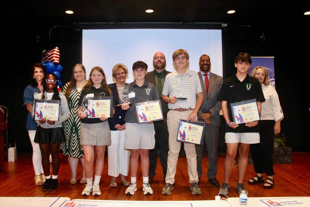 A stage full of teens holding up National Civics Bee certificates