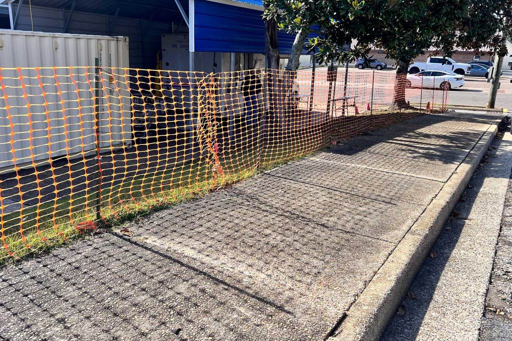 A plastic orange safety fence is hung along a sidewalk in front of a metal overhang