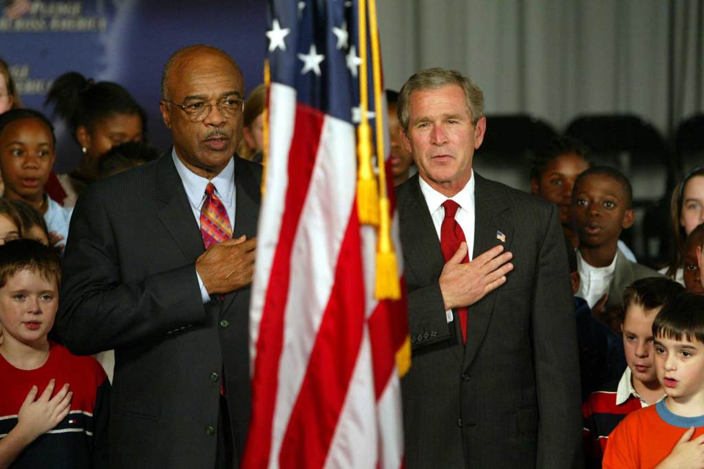 Rod Paige and George W Bush stand and lead the Pledge of Allegiance with a crowd of children