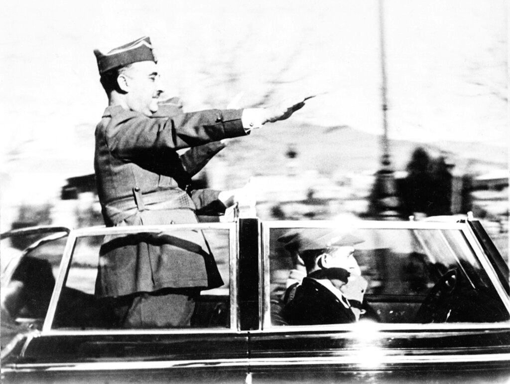 A black-and-white photo of Francisco Franco in military dress, saluting a crowd