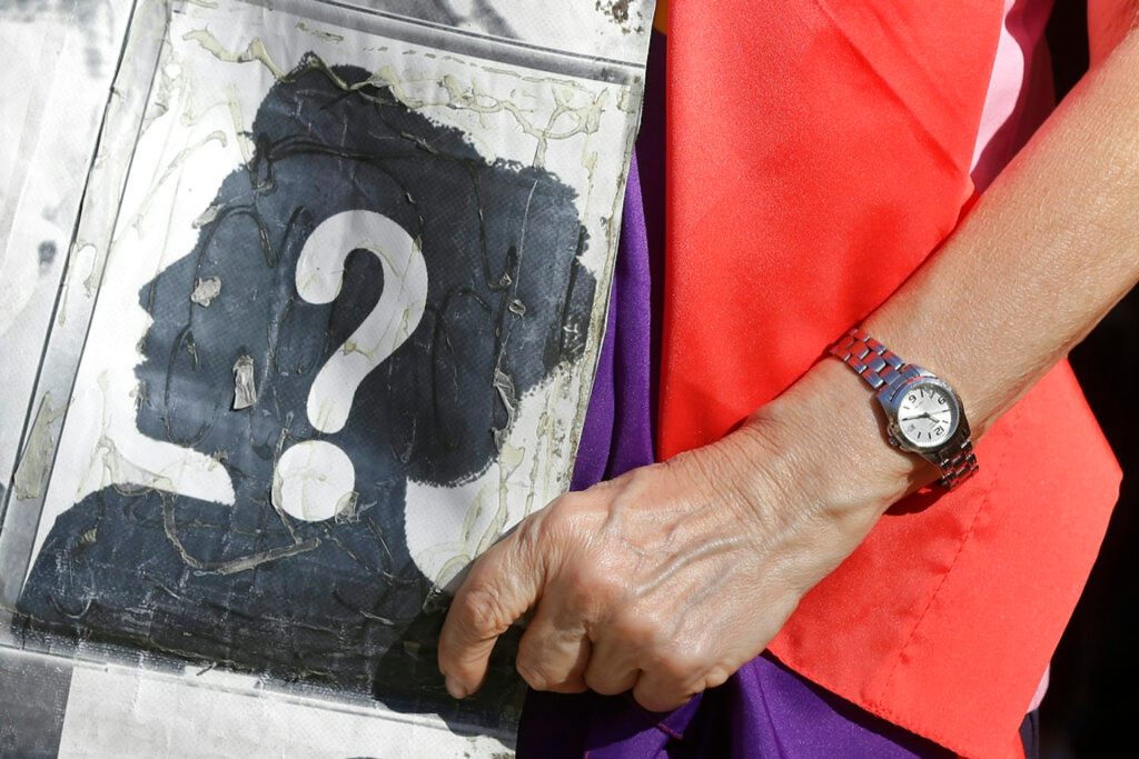 A woman’s hand holding a poster. The poster has the silhouette of a woman with a question mark on it.