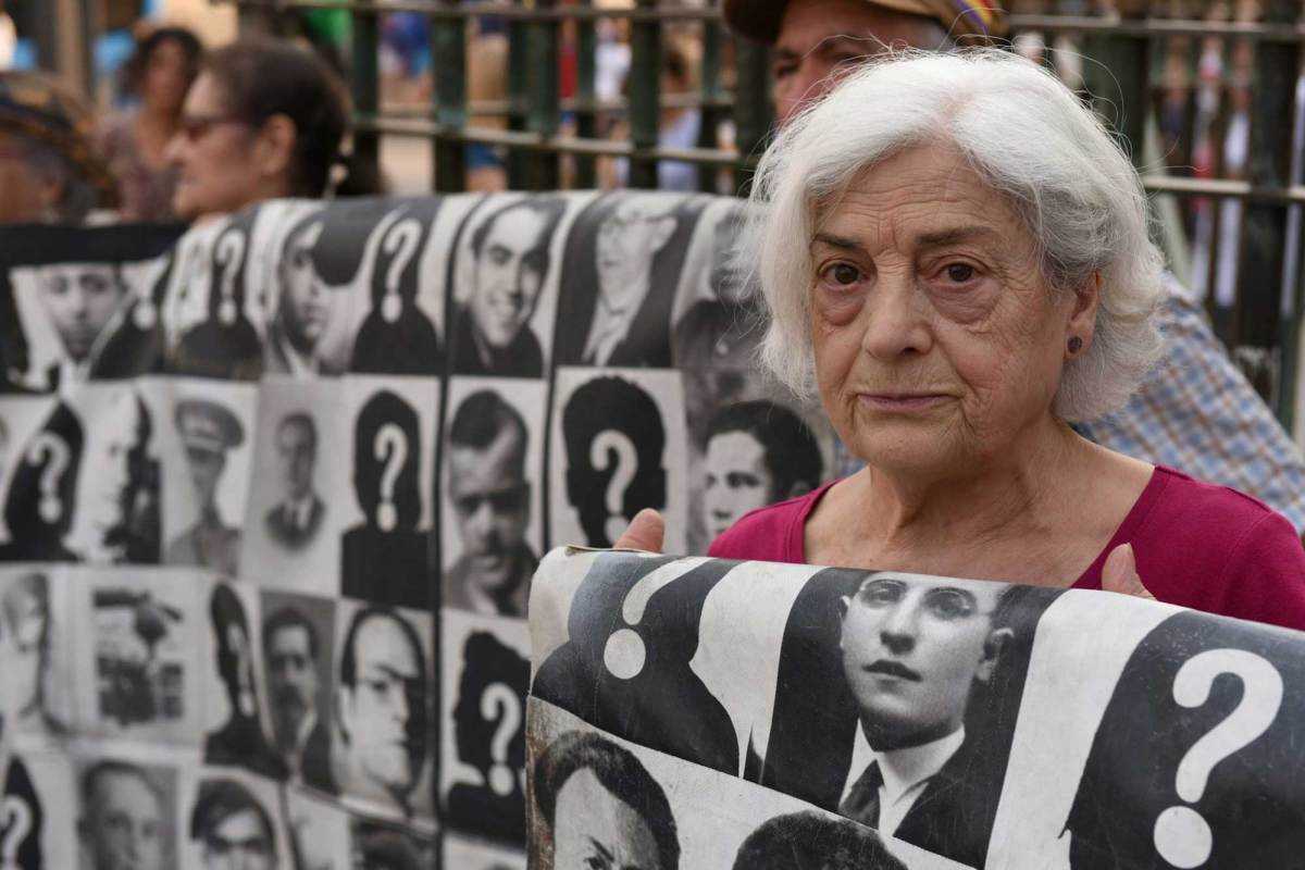 A woman holds a blanket with black-and-white pictures of people who went missing during the Spanish dictatorship of Francisco Franco