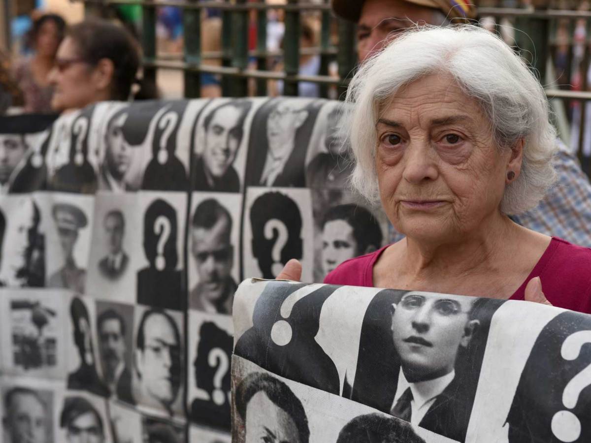 A woman holds a blanket with black-and-white pictures of people who went missing during the Spanish dictatorship of Francisco Franco
