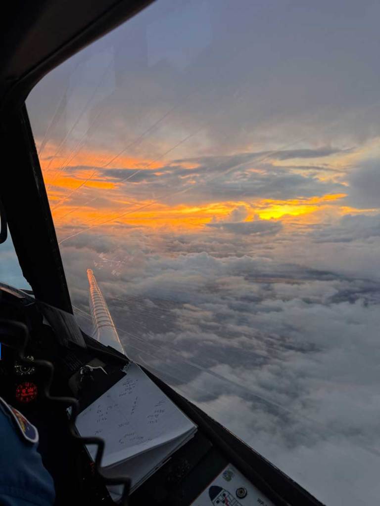 A cloud strewn sunset as seen out of an airplane cockpit window