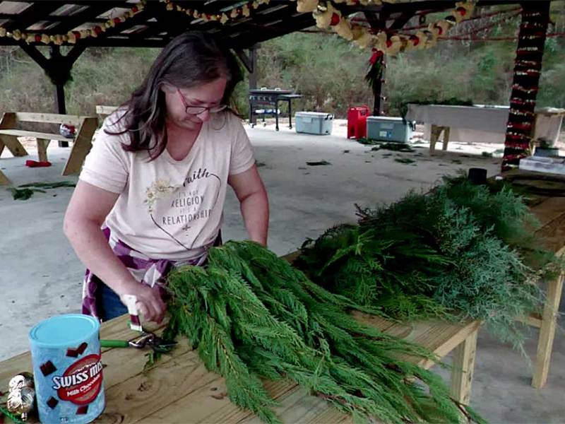Hope Cooley arranging evergreen branches on a worktable at an outdoor farm workspace.