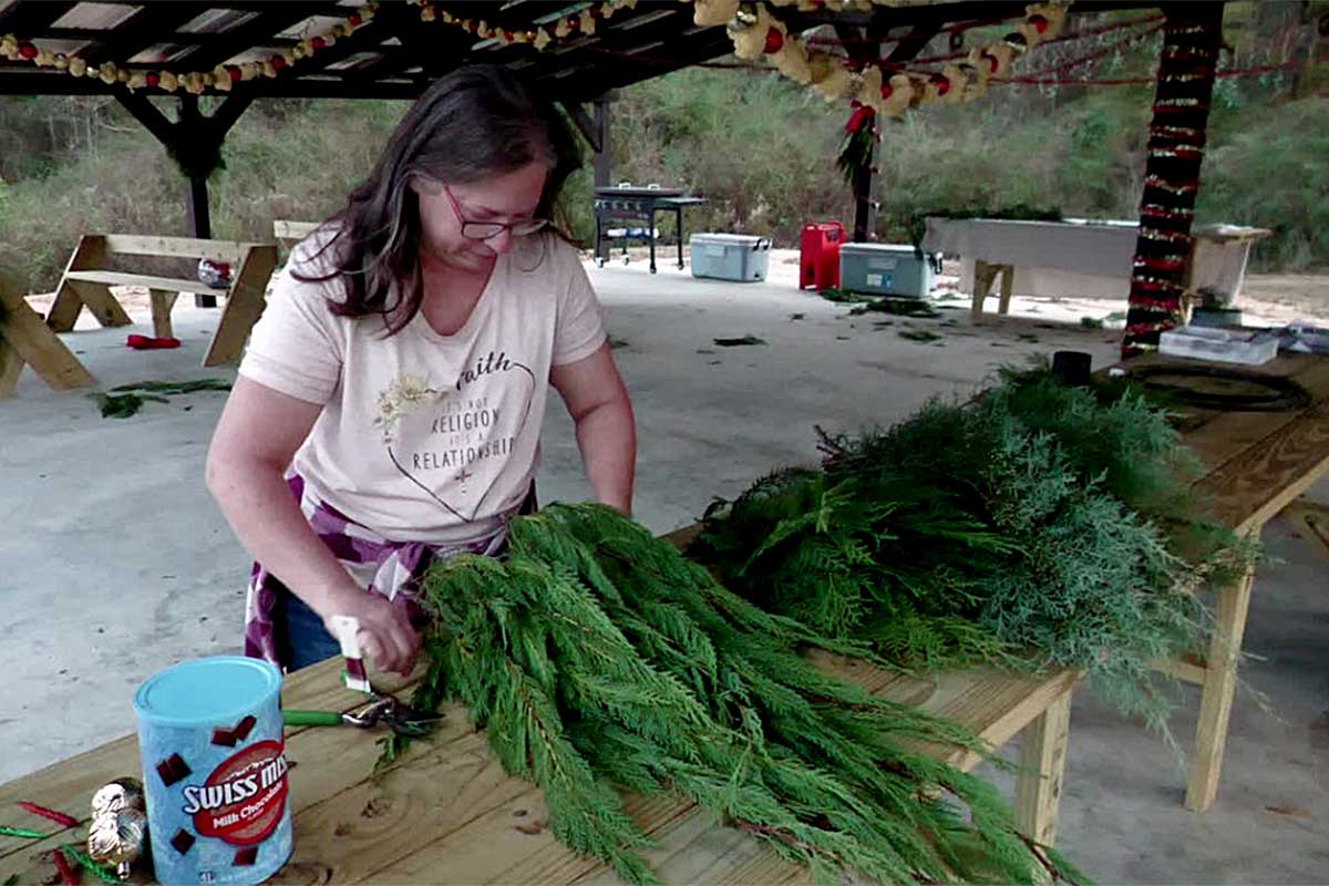 Hope Cooley arranging evergreen branches on a worktable at an outdoor farm workspace.